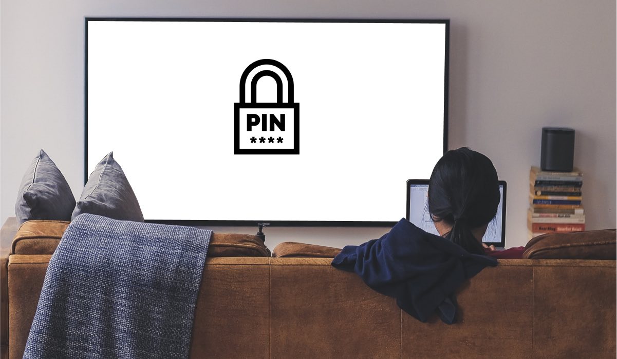 A person sitting on a couch watching TV. the Tv has the PIN graphic with a locket