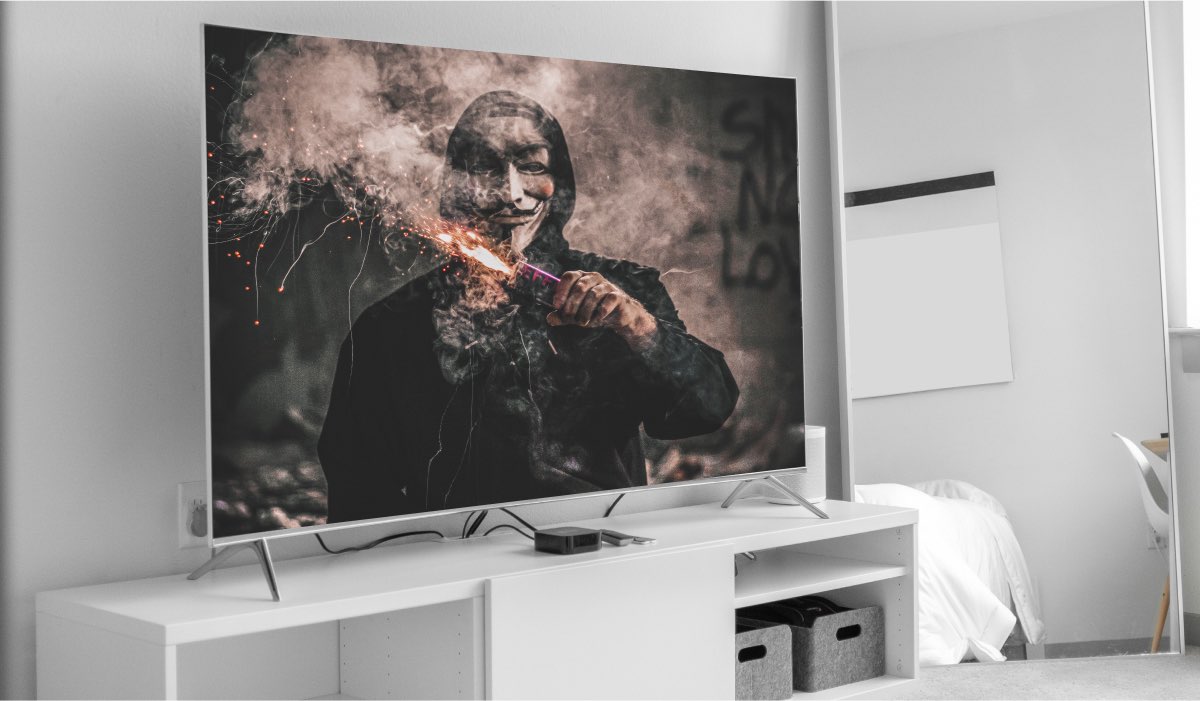 An image of a person in Anonymous mask and a smoke candle in hand on a LG Tv screen. The TV is standing on a white drawer