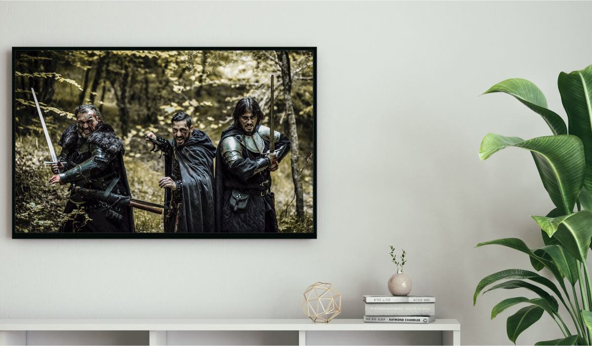 A tv hanging in a living room with three men dressed in warrior armor. There's a drawer and a house plant