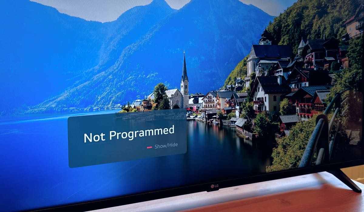 LG Tv screen with an image of a city by a lake in the mountains. There is a pop-up screen with a message "Not Programmed" on the screen