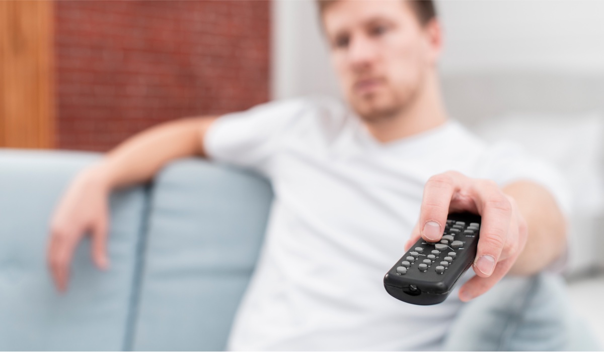 A man is sitting on a couch, pointing a remote at something