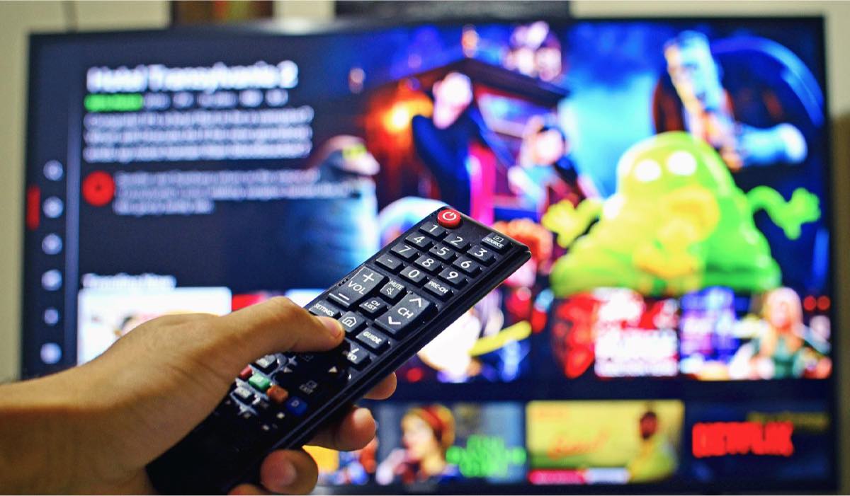 a hand holding an LG remote, pointing it at a TV with a streaming app on the screen