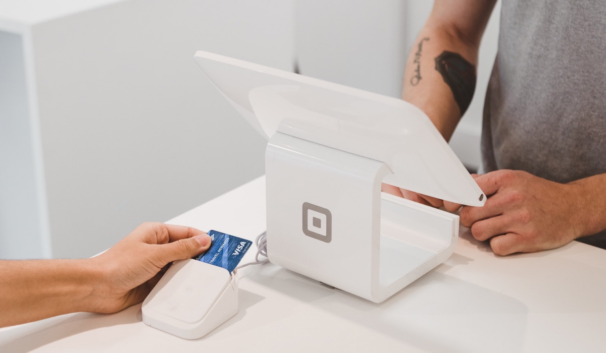 A person using a card terminal to pay. Another person stands by a till.