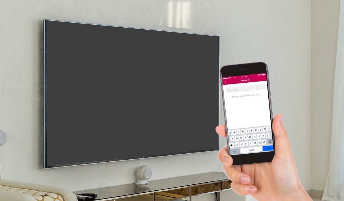 A hand holding an iPhone with the LG TV Remote Control Plus app on the screen. In the background there's an LG TV with black screen