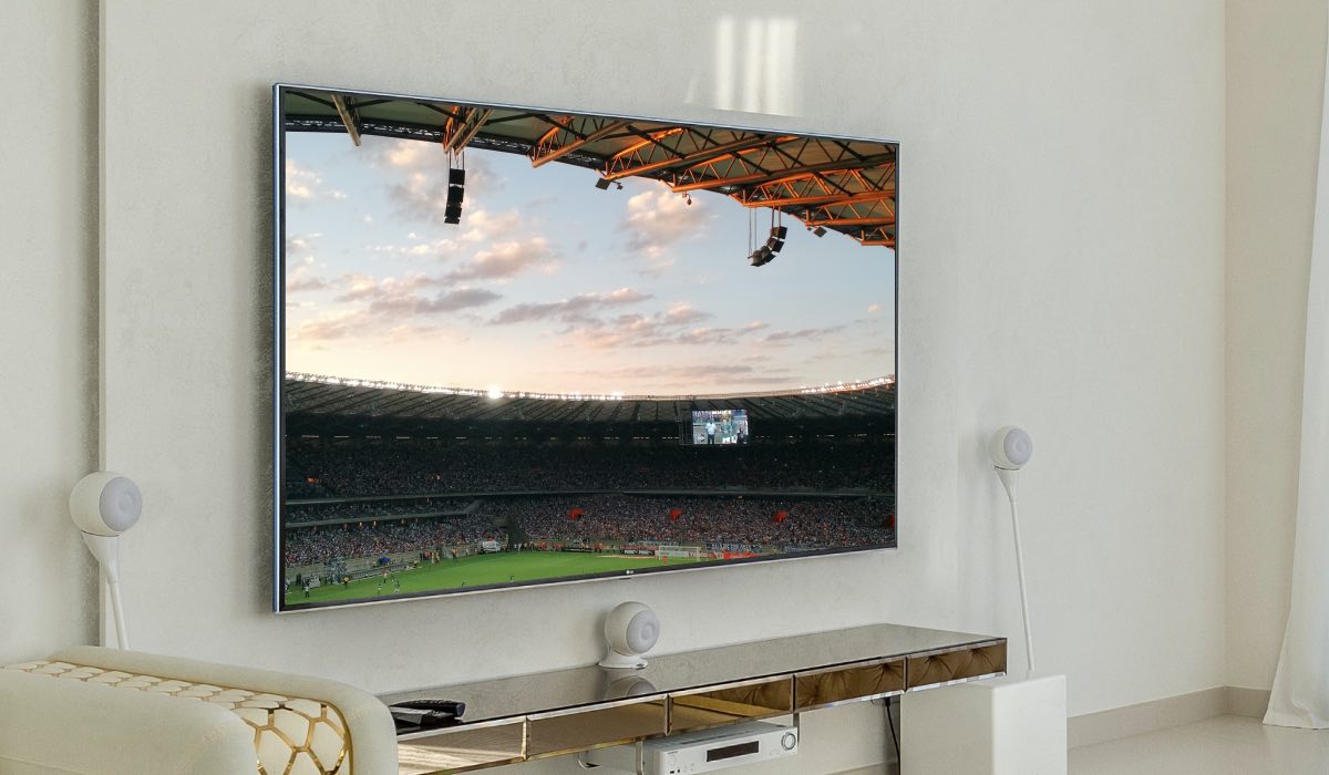 An LG TV hanging on a wall below a shelf. The TV screen is displaying a football stadium