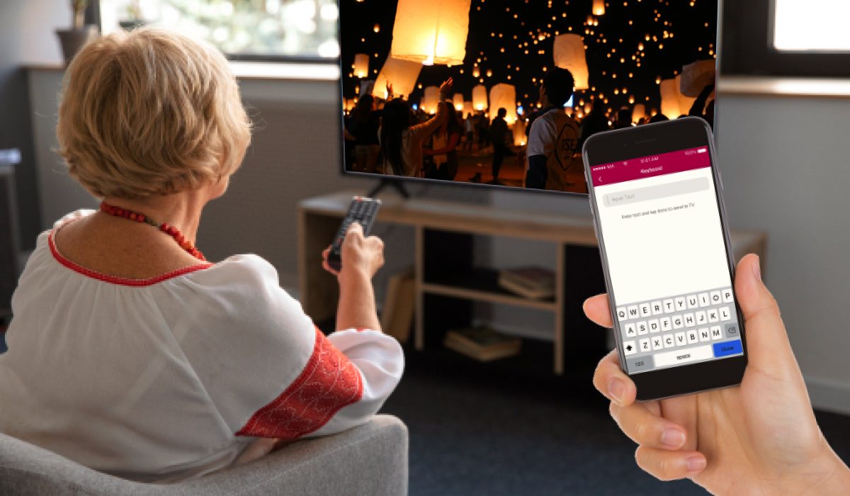 A person watching video of a fireplace on a TV. A hand holding an iPhone with the LG TV Remote Control Plus interface on the screen.