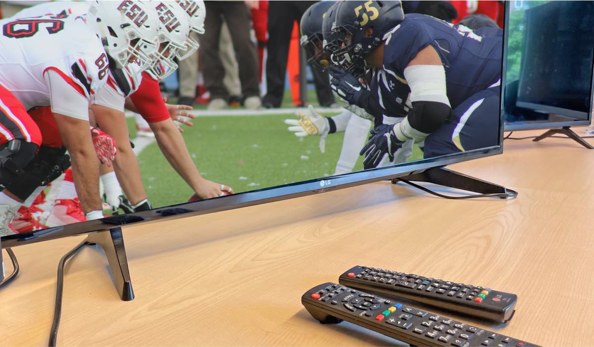 LG TV with american football match on the screen. Two remotes - a normal LG TV remote and a Magic Remote.