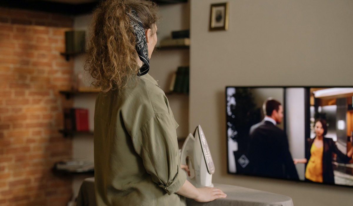 A woman with a bandana around her head and a cleaning rag in her hand is watching a TV series on an LG TV