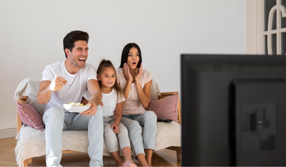 A family of man, daughter and mom watch TV enthusiastically. They're all wearing white