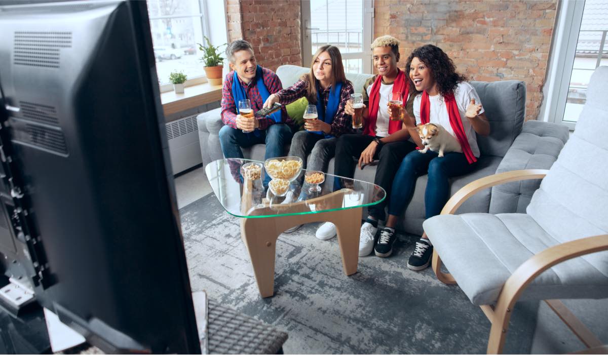 A group of 4 friends watch Tv with snacks on the table in front of them