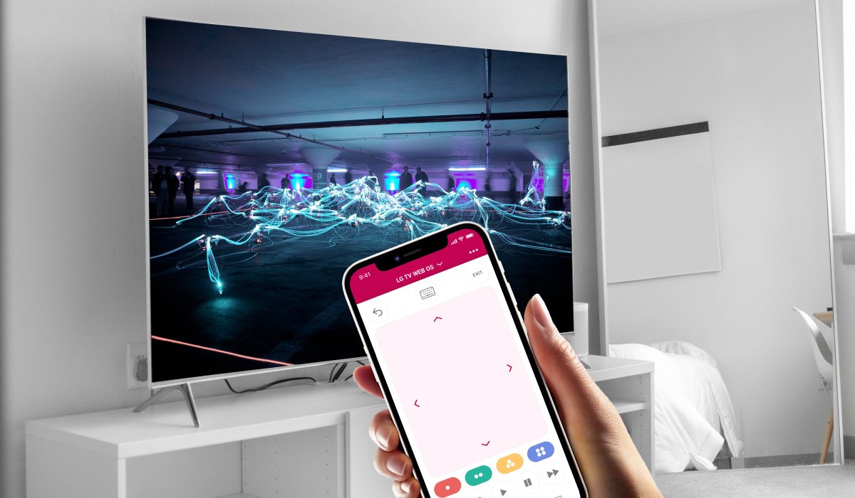 A hand holding an iPhone with the LG TV Remote Control Plus app interface on the screen. An LG TV with electric art installation on the screen. The TV is standing on a white drawer