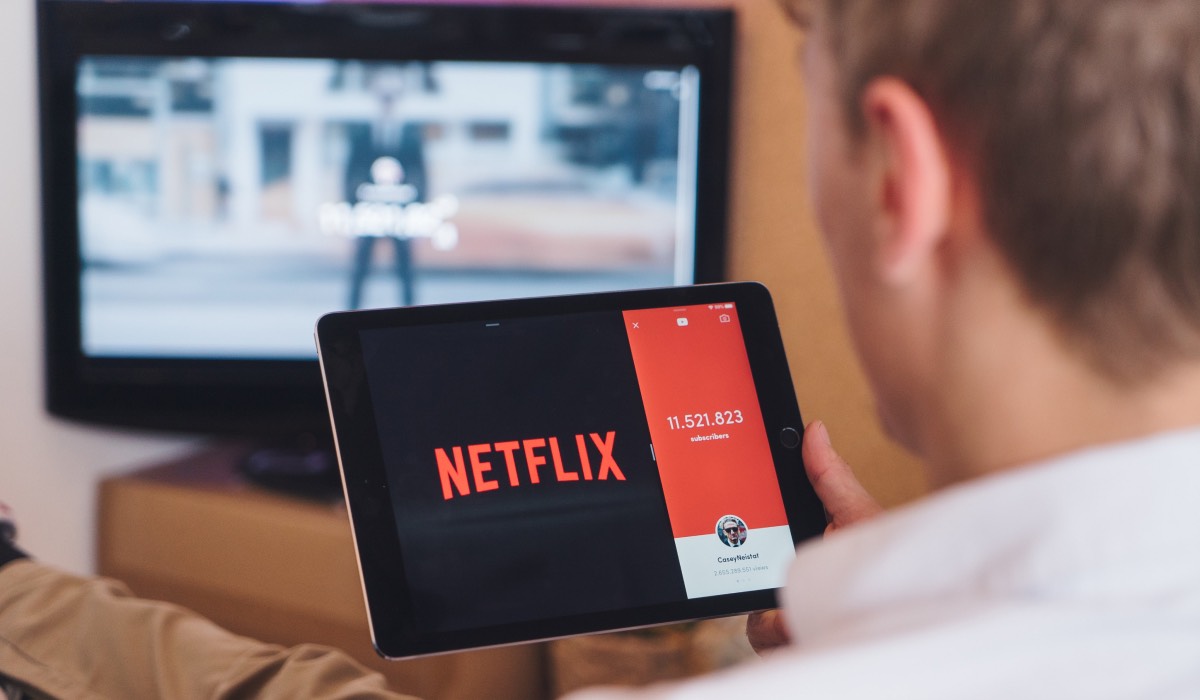 A man holding a tablet with Netflix icon in the screen. An LG TV in a room