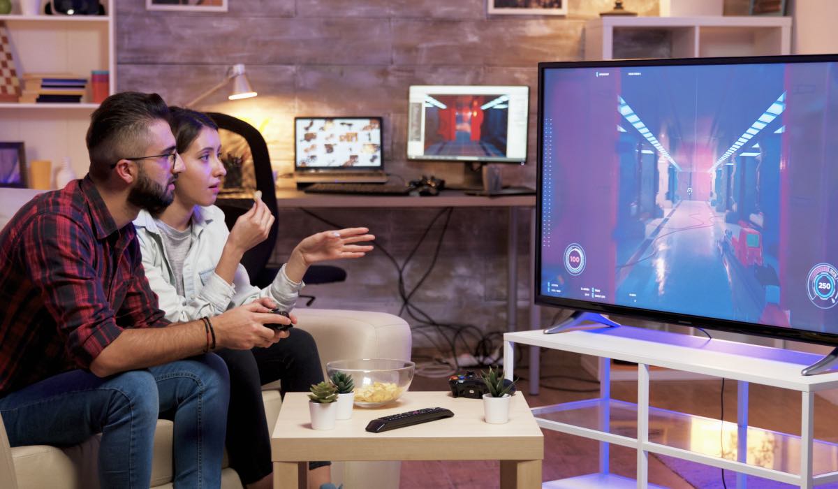 A man and a woman play games on a console. They're in a living room, with a coffee table in front of them
