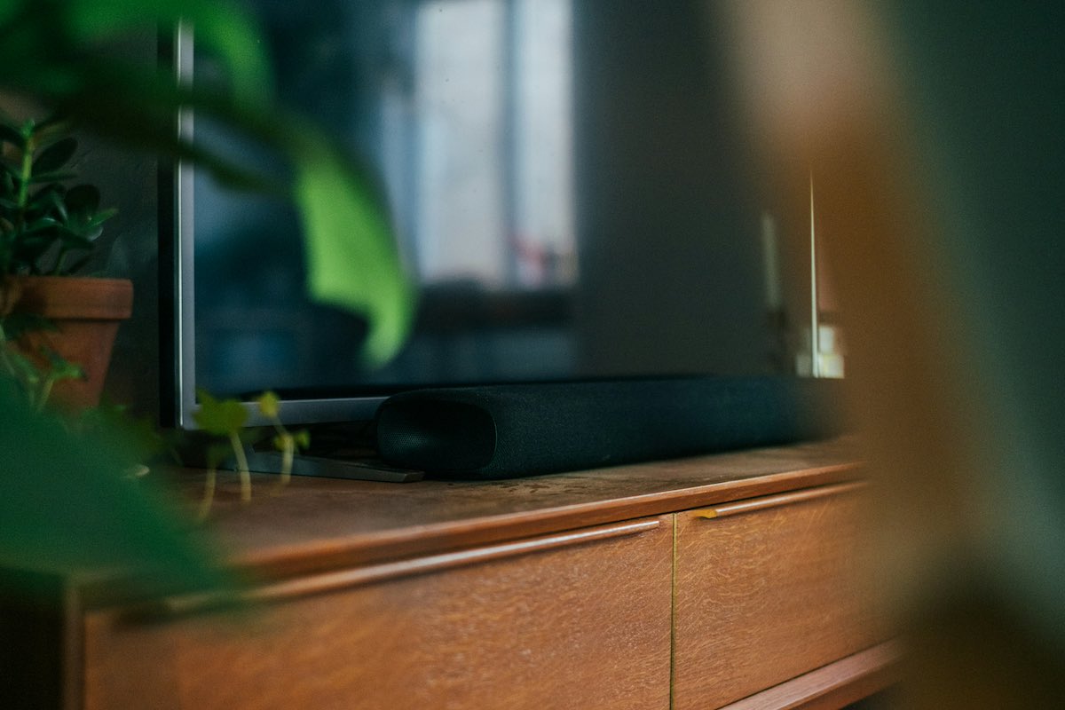 A TV with a soundbar on a wooden drawer. Plants in the foreground