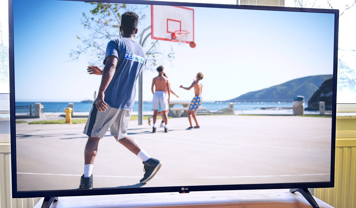 An LG TV in a living room. On the screen: Four men playing basketball by the seaside